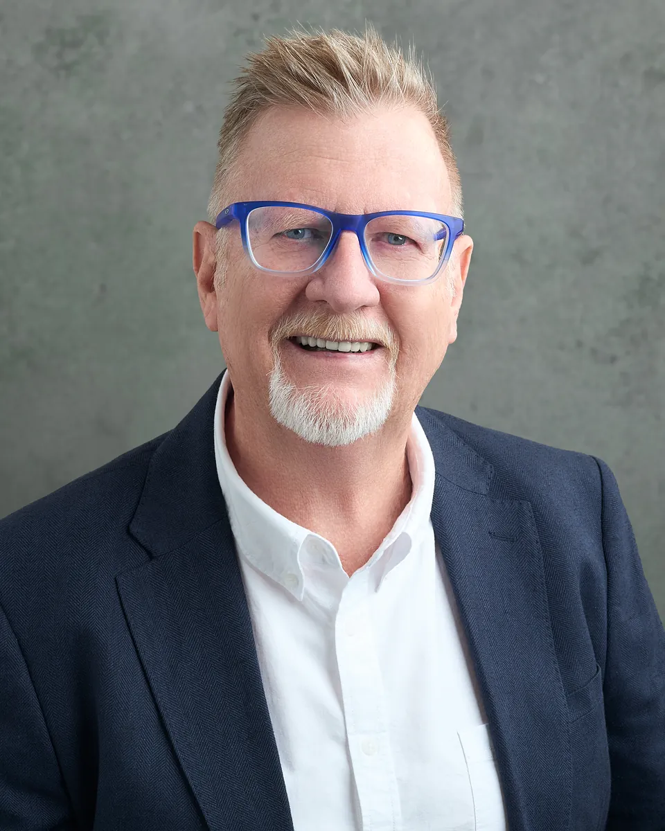 John Musker, smiling, in a navy jacket and blue glasses